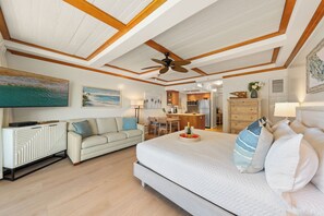 A bedroom with a bed, a sofa, a dining area, and a kitchen.