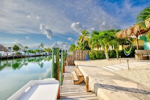 A wooden dock leading to a calm body of water, surrounded by palm trees and a thatched-roof structure. - Trip Around the Sun 2/2 + dockage & Cabana Club (Key Colony Beach)