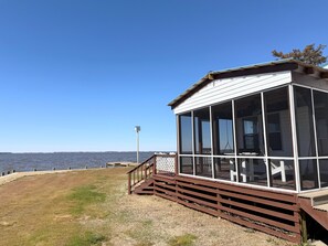 Un edificio frente al agua con un amplio ventanal, una terraza de madera y vistas despejadas al agua.