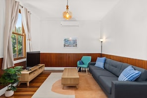 A living room with a TV, sofa, armchair, wooden floor, and a hanging light fixture. - Relaxing Retreat With Spacious Outdoor Area (Newcastle)