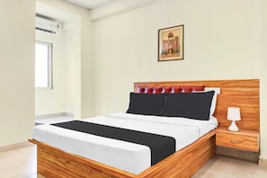 Ein ordentlich bezogenes Bett mit einem Holzkopfstück, ein Nachttisch mit einer Lampe und ein gerahmtes Bild an der Wand.