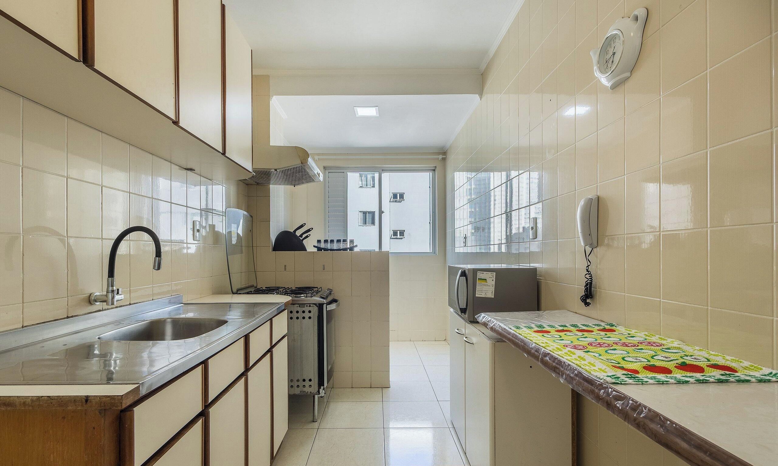 A kitchen with a stainless steel sink, a stove, and a microwave. There is a window with a view of buildings outside.