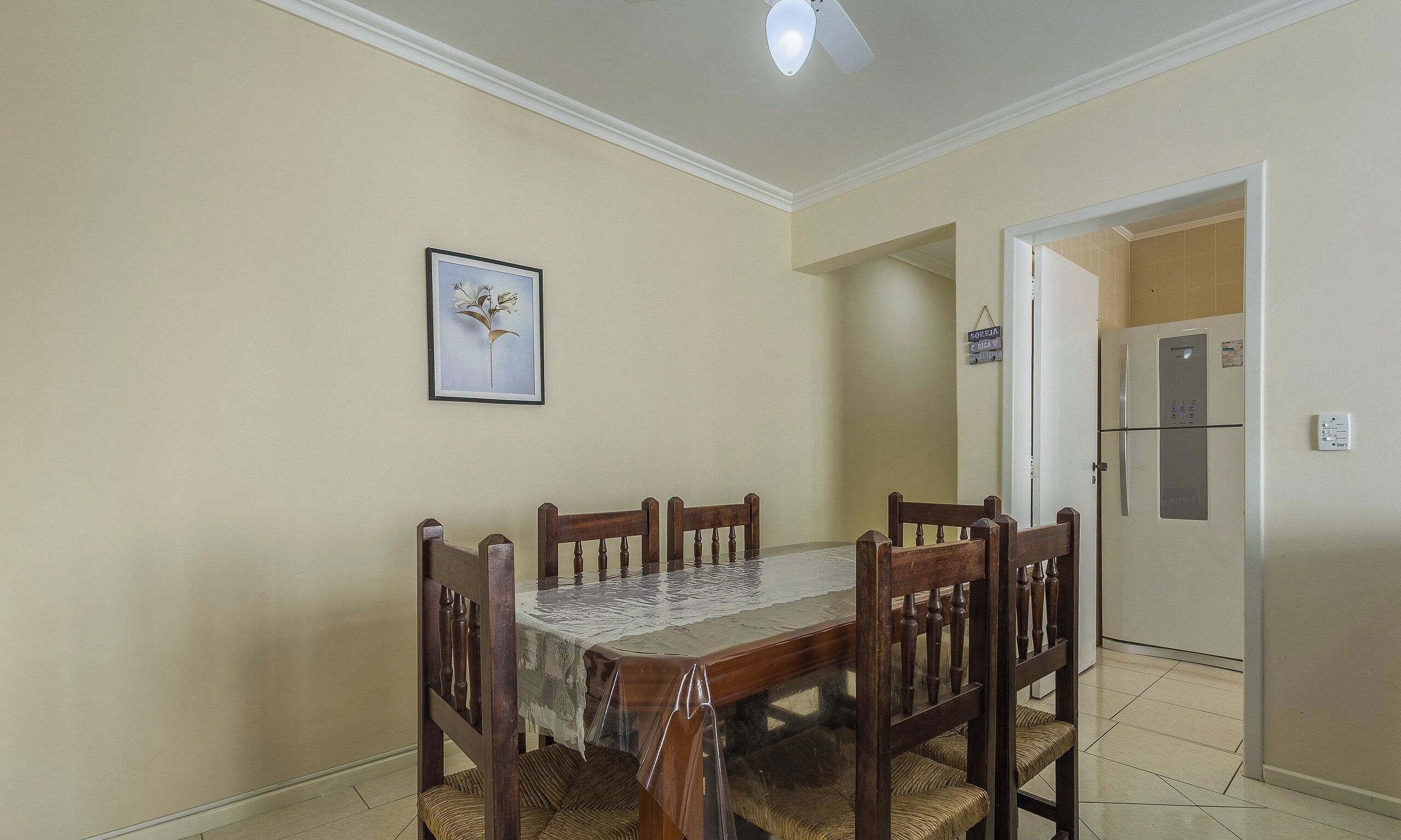 A dining area with a table and chairs, a framed picture on the wall, and a refrigerator in the background.