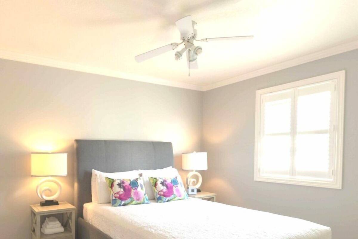 A bedroom with a bed, two bedside tables, a ceiling fan, and a window.