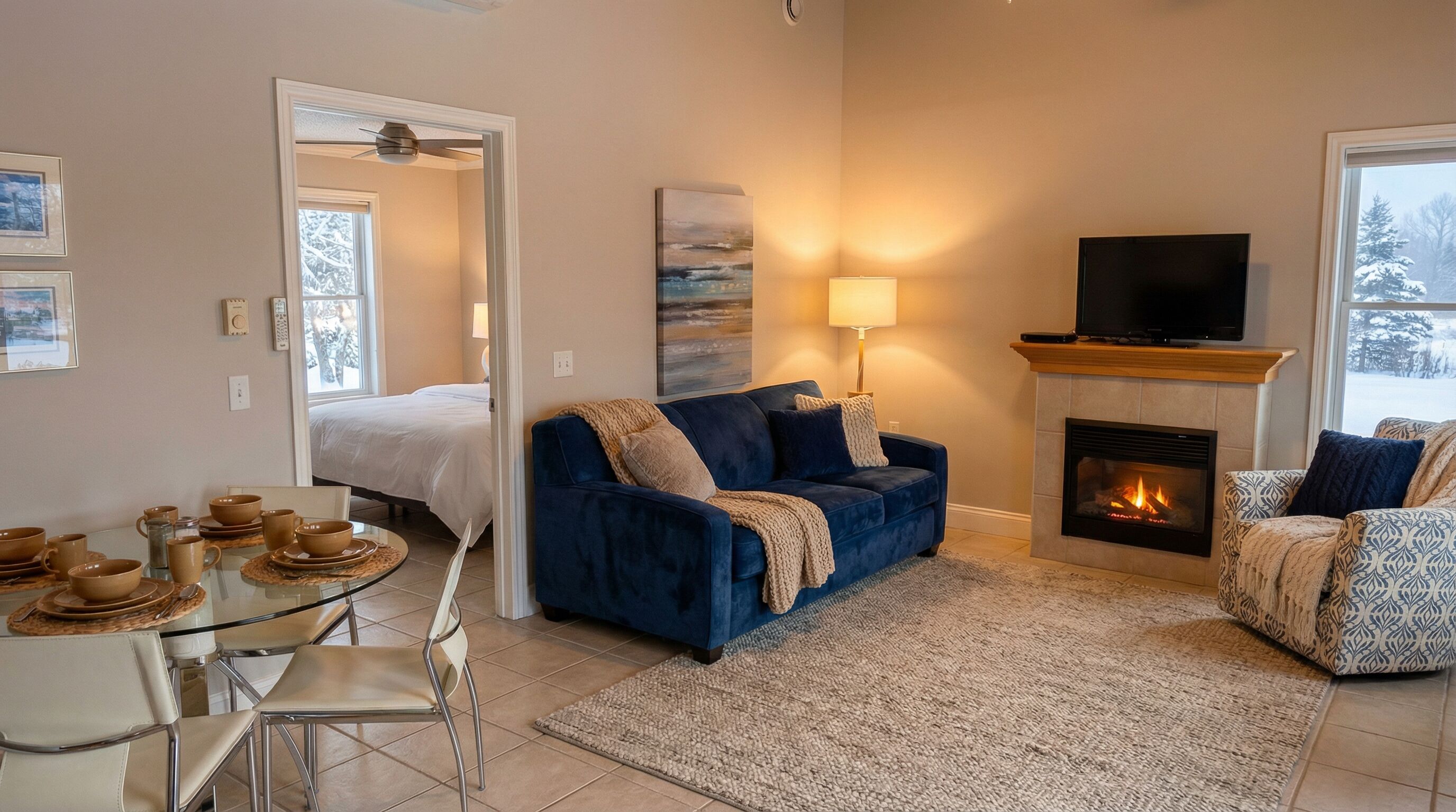 Una sala de estar acogedora con un sofá azul, una chimenea, un televisor y un comedor con una mesa de vidrio y sillas.