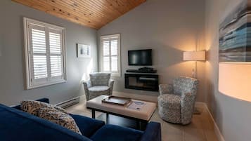 Una sala de estar con un sofá azul, sillones estampados, una mesa de centro con libros, un televisor y una lámpara.