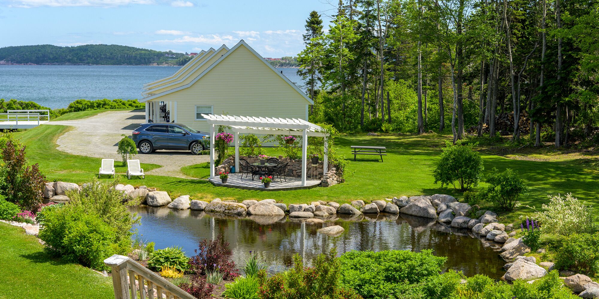 Une propriété située au bord d’un lac, dotée d’un patio couvert, d’un étang et d’une voiture garée devant.
