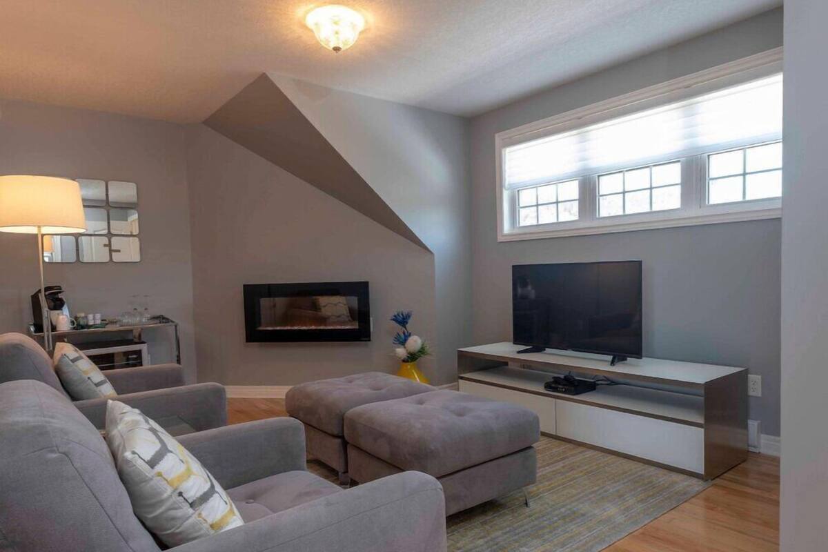 A modern living room with a grey sofa set, a flat-screen TV, and a large window.