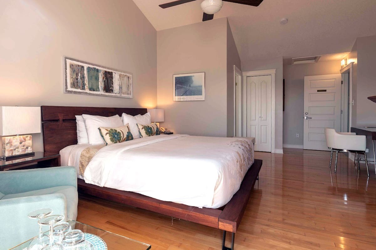 A bedroom with a wooden bed, a nightstand with a lamp, a chair, and a fireplace.