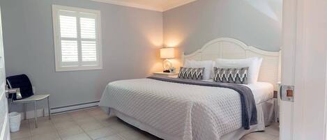 Un dormitorio con cama, mesita de noche, lámpara y una silla.