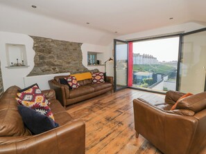Uma sala de estar moderna com sofás de couro, parede de pedra e uma grande porta de vidro que dá para uma varanda com vista.