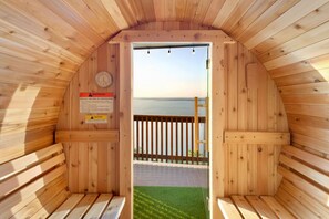 Un sauna en bois avec vue sur la mer, une horloge et un panneau d’avertissement.
