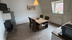 Une cuisine compacte avec un coin repas, un réfrigérateur, un four à micro-ondes et une fenêtre donnant sur un bâtiment au toit rouge.