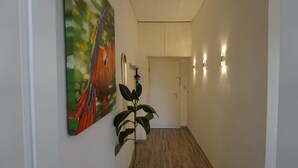 Un couloir avec un plancher en bois, une plante en pot et un tableau accroché au mur.