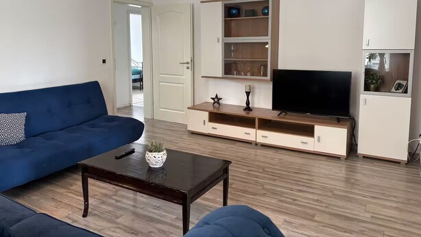 Un salon avec un canapé bleu, une table basse en bois foncé, un téléviseur et un meuble avec des étagères.