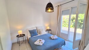 Ein Schlafzimmer mit einem Bett, zwei Nachttischen mit Lampen, einem Fenster mit Jalousien und Blick ins Grüne.