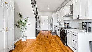 A modern kitchen with white cabinetry, a wooden floor, and a potted plant.