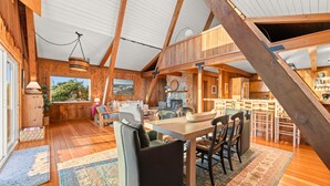 A spacious loft with high ceilings, wooden beams, a dining area with a long table and chairs, a kitchen area, and a large window overlooking a scenic landscape. - 25% Off Sept 7-9, On The Sand Perfect 4 Families! (Ventura)