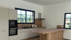 A modern kitchen with a central island, built-in oven, and large windows. - Villa 8 people - Peace & comfort (Ghisonaccia)