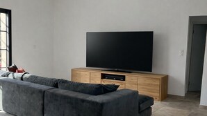 A modern living room with a large sectional sofa, a flat-screen TV on a wooden cabinet, and a tiled floor. - Villa 8 people - Peace & comfort (Ghisonaccia)