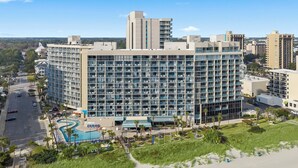 Ein mehrstöckiges Hotel mit Poolanlage, umgeben von einem angelegten Garten und einem Sandstrand.