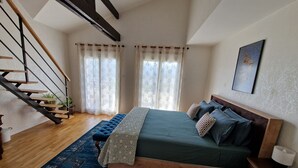 A bedroom with a wooden bed, a blue rug, a staircase, and a window with curtains. - guest room overlooking the town of Lourdes and splendid view of the Pyrenees (Lourdes)