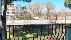 A balcony with a metal railing overlooking a landscaped area with trees and a building in the background. - Bright Apartment With Pool (Cavallino-Treporti)