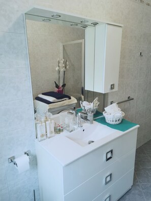 A bathroom with a white sink, mirror, and storage cabinet. There are toiletries on the counter, a towel, and a vase with flowers. - VSM 108 Perfect location for Venice, ideal for families and free parking (Venezia-Mestre)