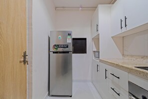 Una cocina compacta con refrigerador de acero inoxidable, gabinetes blancos y encimera de granito.