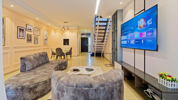Una sala de estar moderna con un sofá, un reposapiés y un televisor de pantalla plana montado en la pared.