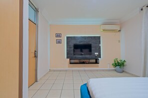 Ein Hotelzimmer mit Bett, Wandfernseher, Blumentopf und Tür.