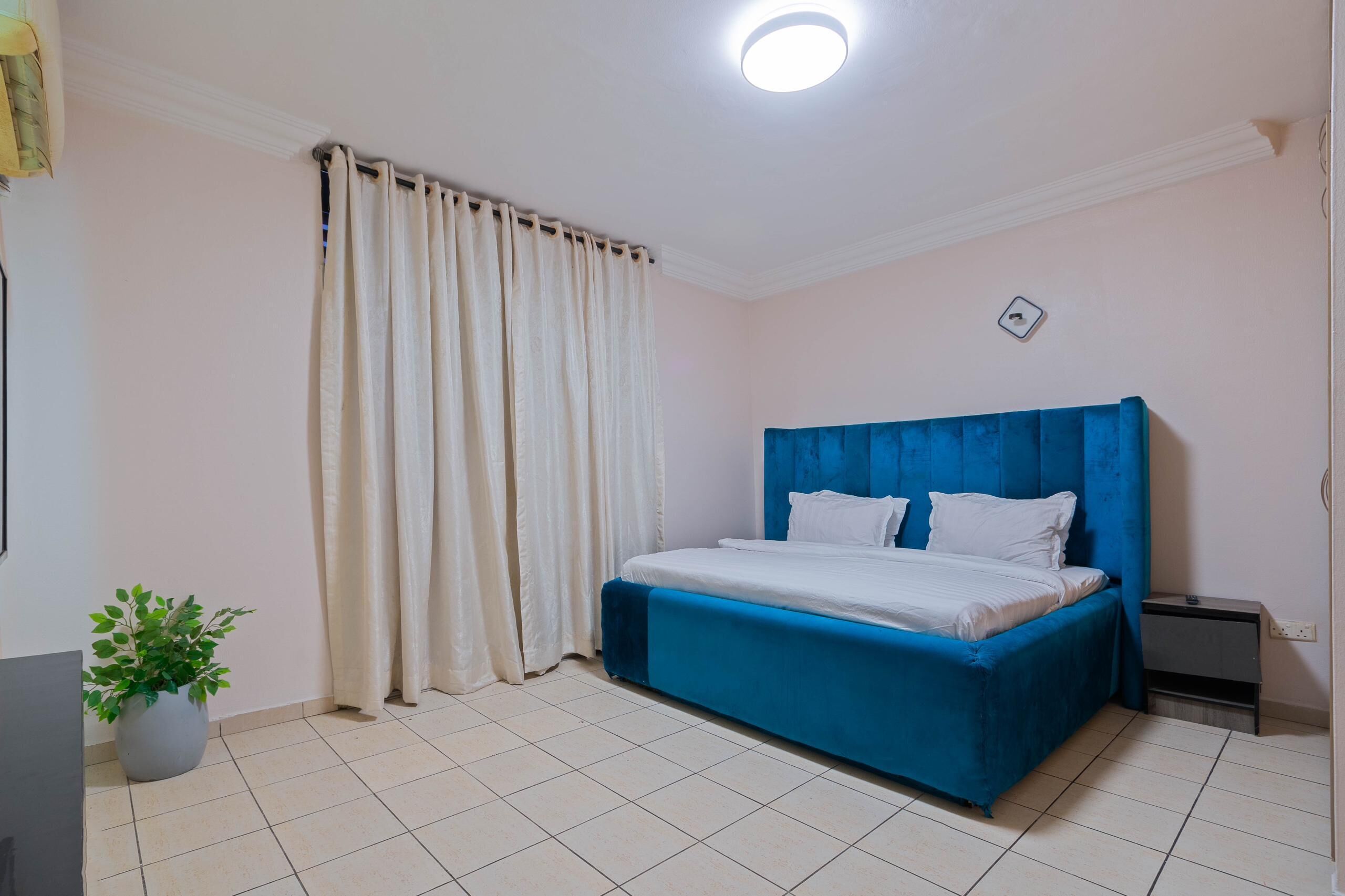 A bedroom with a bed, curtains, a potted plant, and a nightstand.