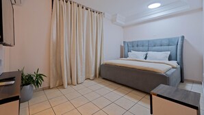 Un dormitorio con cama, cortinas, una planta en maceta, un escritorio y una lámpara de techo.