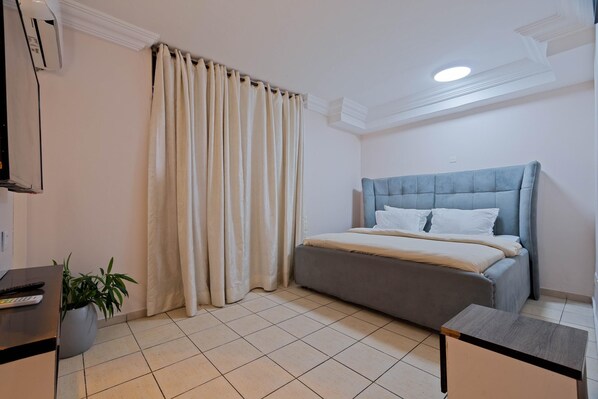 Un dormitorio con cama, cortinas, una planta en maceta, un escritorio y una lámpara de techo.