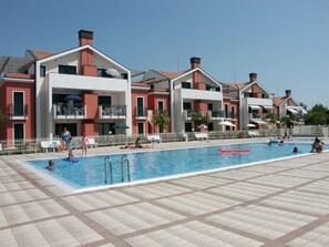 A swimming pool area with tiled flooring, a pool, and a building with balconies and outdoor seating. - Apartment With Terrace and Pool (Cavallino-Treporti)