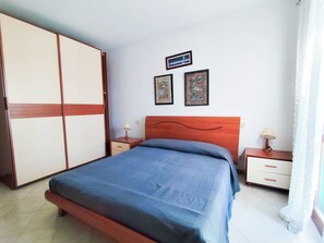 Quarto com cama, mesa de cabeceira, penteadeira e duas fotos emolduradas na parede.