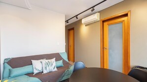 A room with a brown sofa, two teal pillows, a wooden door, and an air conditioning unit. - Modern apt in Sudoeste w/ A/C & Wi-fi Cls0101 (Sudoeste e Octogonal)