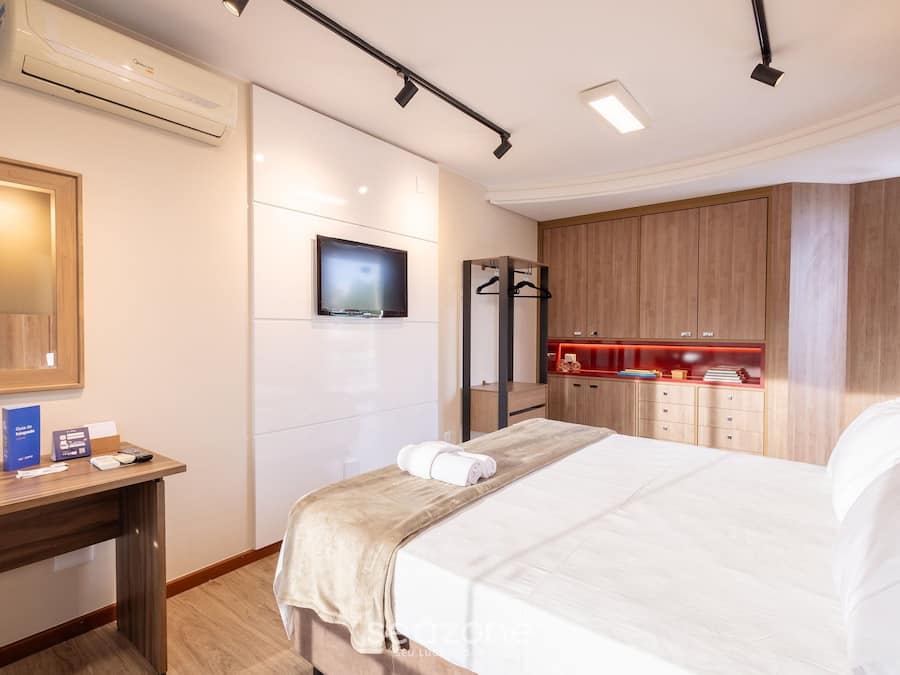 Hotellihuone, jossa on sänky, työpöytä, televisio, peili ja vaatekaappi.