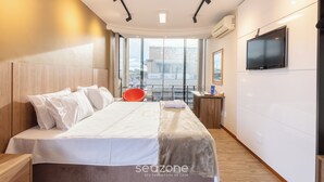 A modern hotel room with a large bed, a TV mounted on the wall, and a view of the city through large windows. - Modern apt in Sudoeste w/ A/C & Wi-fi Cls0101 (Sudoeste e Octogonal)
