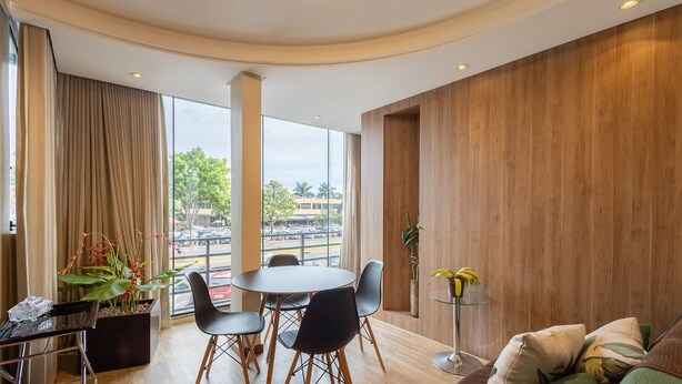 A modern hotel room with a curved ceiling, large windows offering a city view, a round dining table with chairs, and a small side table with a plant. - Modern apt in Sudoeste w/ A/C & Wi-fi Cls0101 (Sudoeste e Octogonal)