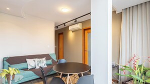 A modern living room with a sofa, a round table, and chairs. There is a door and an air conditioning unit on the wall. - Modern apt in Sudoeste w/ A/C & Wi-fi Cls0101 (Sudoeste e Octogonal)