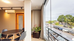 A modern hotel room with a balcony, a round table with chairs, a potted plant, and a view of a busy street and parking lot. - Modern apt in Sudoeste w/ A/C & Wi-fi Cls0101 (Sudoeste e Octogonal)