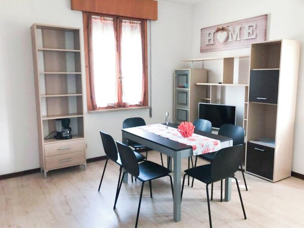 A modern living room with a dining table, chairs, a coffee machine, and built-in shelving. - Comfy Bungalow With Garden (Cavallino-Treporti)