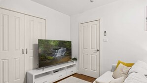 Ein Wohnzimmer mit einem Flachbildfernseher auf einer weißen Unterhaltungseinheit, einem weißen Sofa mit gelben Kissen und weißen Türen.