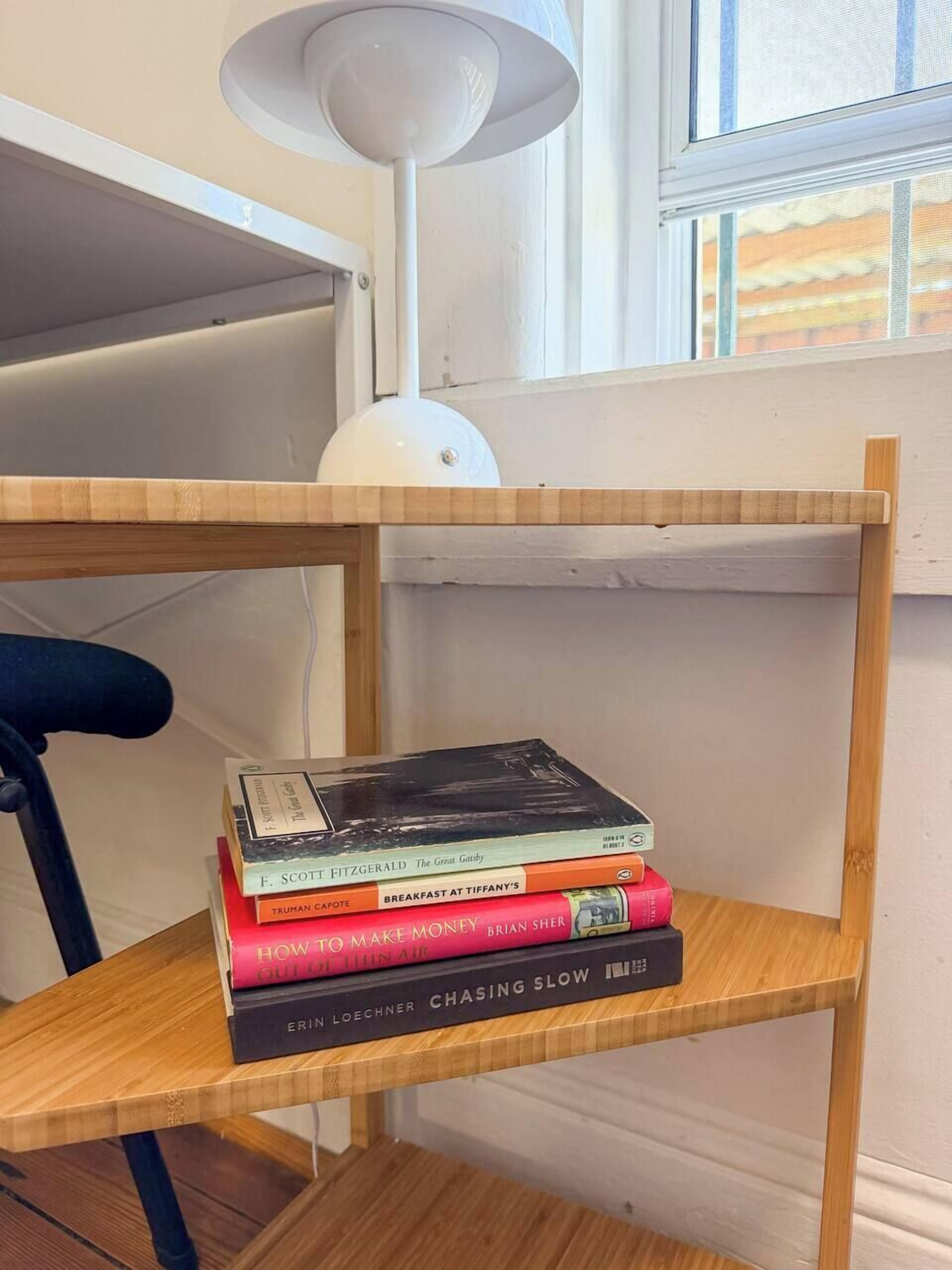 A wooden shelf with a stack of books, a white lamp, and a chair.