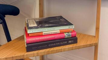 A wooden shelf with a stack of books, a white lamp, and a chair.
