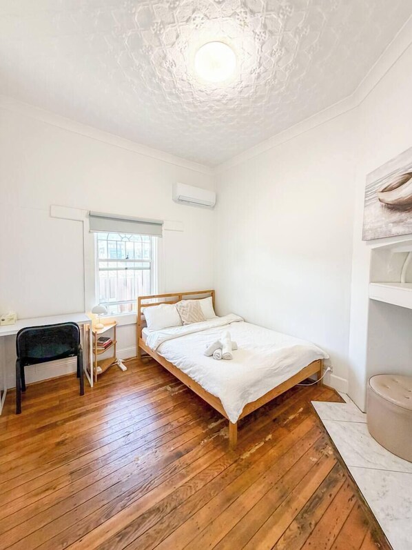 Un dormitorio con cama de madera, un escritorio con silla, una ventana y un equipo de aire acondicionado.