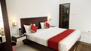 Una habitación de hotel con una cama grande, mesitas de noche, una lámpara de noche, una colcha roja y blanca, y un cabecero de madera.