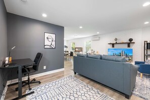 Ein modernes Wohnzimmer mit einem grauen Sofa, einem schwarzen Bürostuhl und einem Teppich mit Muster.
