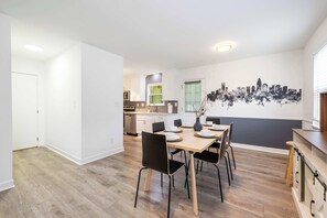 Eine moderne Küche mit weißen Schränken, ein Essbereich mit Holztisch und Stühlen sowie ein Stadtbild-Wandgemälde.